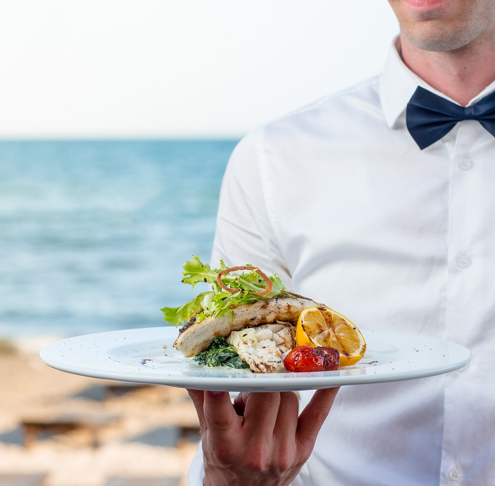 54-waiter-holding-grilled-fish-with-lemon-tomato-creamy-herbs-seaside-restaurant.jpg