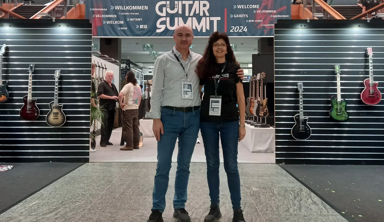 <img src=”Tremoline-GuitarSummit2024-1280x741-v01” width="1280" height="741" alt=”Two people before guitar stand” />