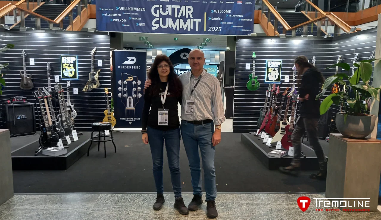 <img src=”Tremoline-GuitarSummit2025-1280x741-v01a” width="1280" height="741" alt=”Two people before guitar stand” />