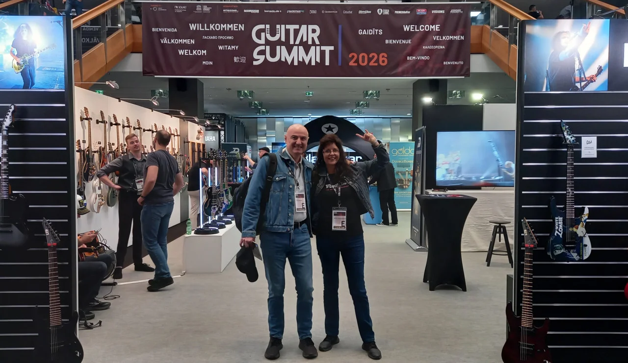 <img src=”Tremoline-GuitarSummit2026-1280x741-S01A” width="1280" height="741" alt=”Two people before guitar stand” />