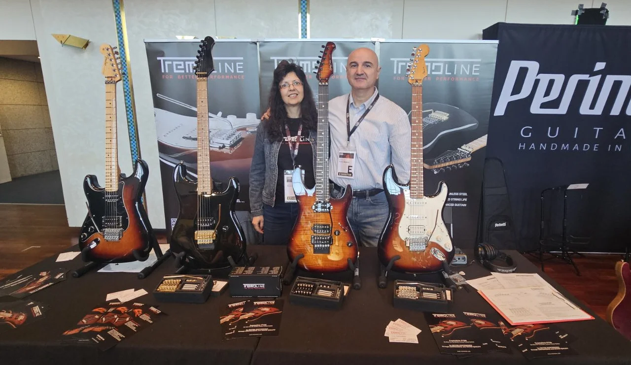 <img src=”Tremoline-GuitarSummit2026-1280x741-S02A” width="1280" height="741" alt=” Two people near to guitar stand” />